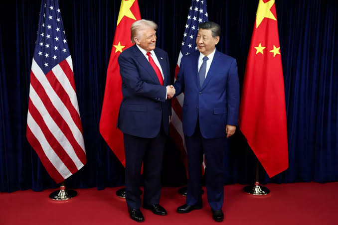 Two officials in dark suits shaking hands between United States and Chinese flags